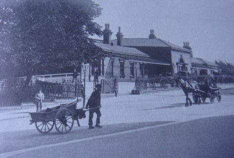 An old photograph of Ilkley's railway station in the 1860s. In the foreground is a boy/young man pulling a wooden cart.